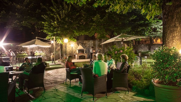 An outdoor patio area with wicker furniture and umbrellas, surrounded by greenery and stone flooring.