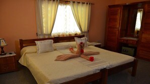 Una cama bien hecha con toallas dispuestas en forma de corazón, una lámpara de noche y un armario de madera.