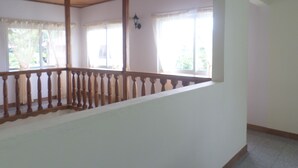 Una habitación con techo de madera, un balcón con barandilla de madera y amplias ventanas con cortinas.