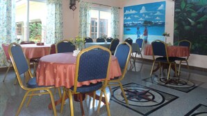 Un comedor con mesas redondas, sillas azules y un mural con una escena de playa.