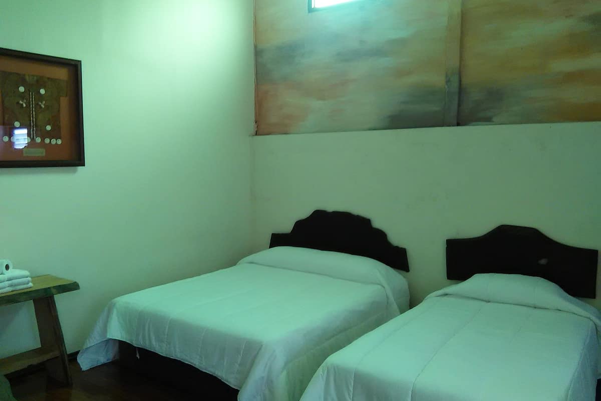 A room with two single beds, a small table with a chair, and a framed picture on the wall.