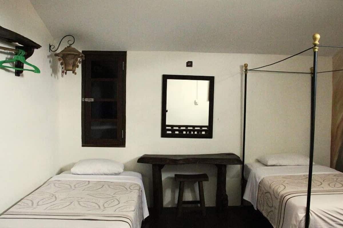 A room with two single beds, a small table, a mirror, and a hanging light fixture.