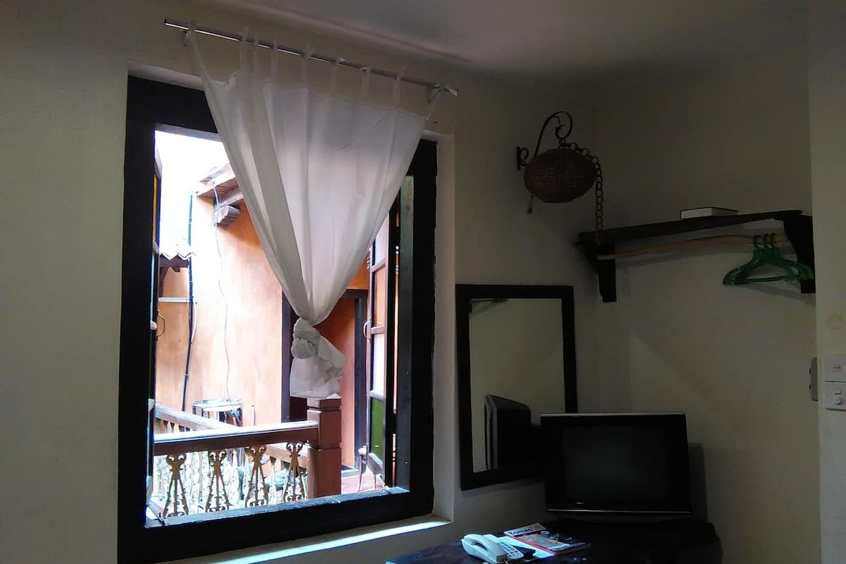 A room with a window, a small table with a telephone and magazines, a television, and a mirror on the wall.