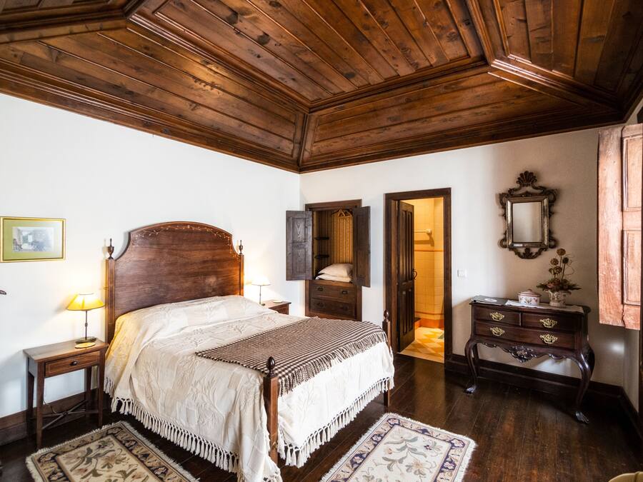 A traditional room with a wooden ceiling, a bed with a headboard, a nightstand, a dresser, and a mirror.