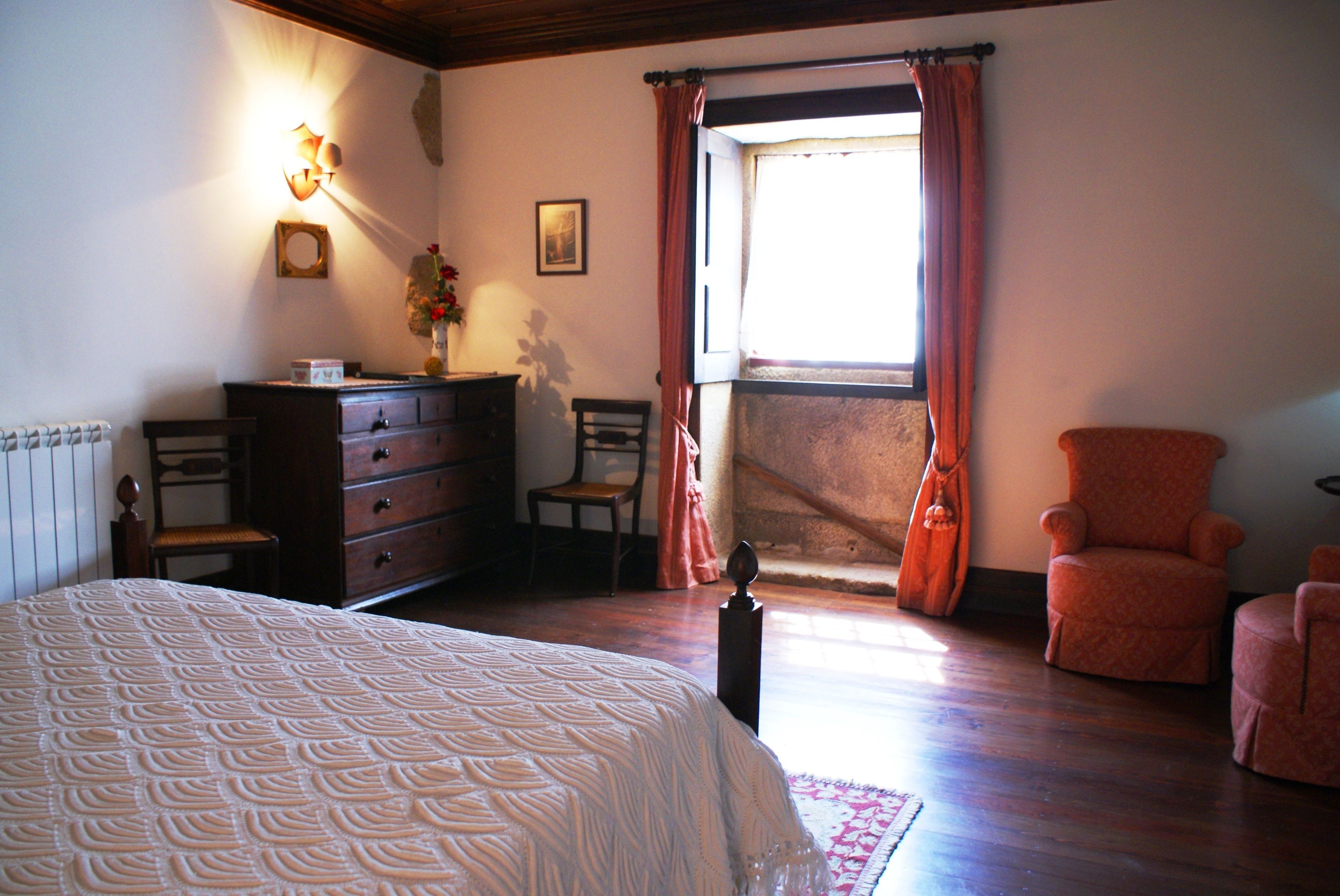 A bedroom with a bed, dresser, chair, and a window with curtains.