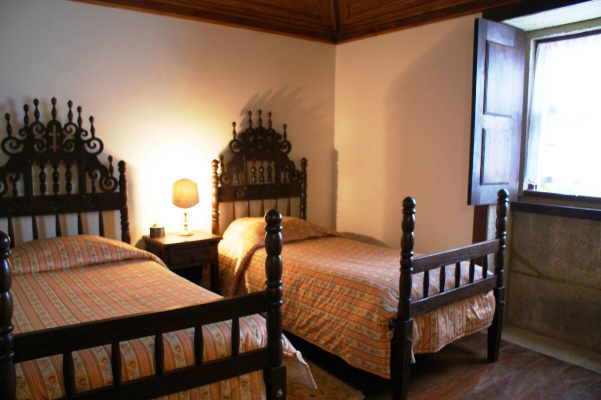 A bedroom with two wooden beds, a nightstand, and a window with a view.