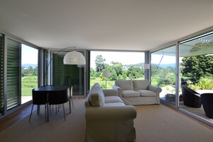 Una sala de estar moderna con un sofá, una mesa y vistas a un viñedo a través de amplios ventanales.