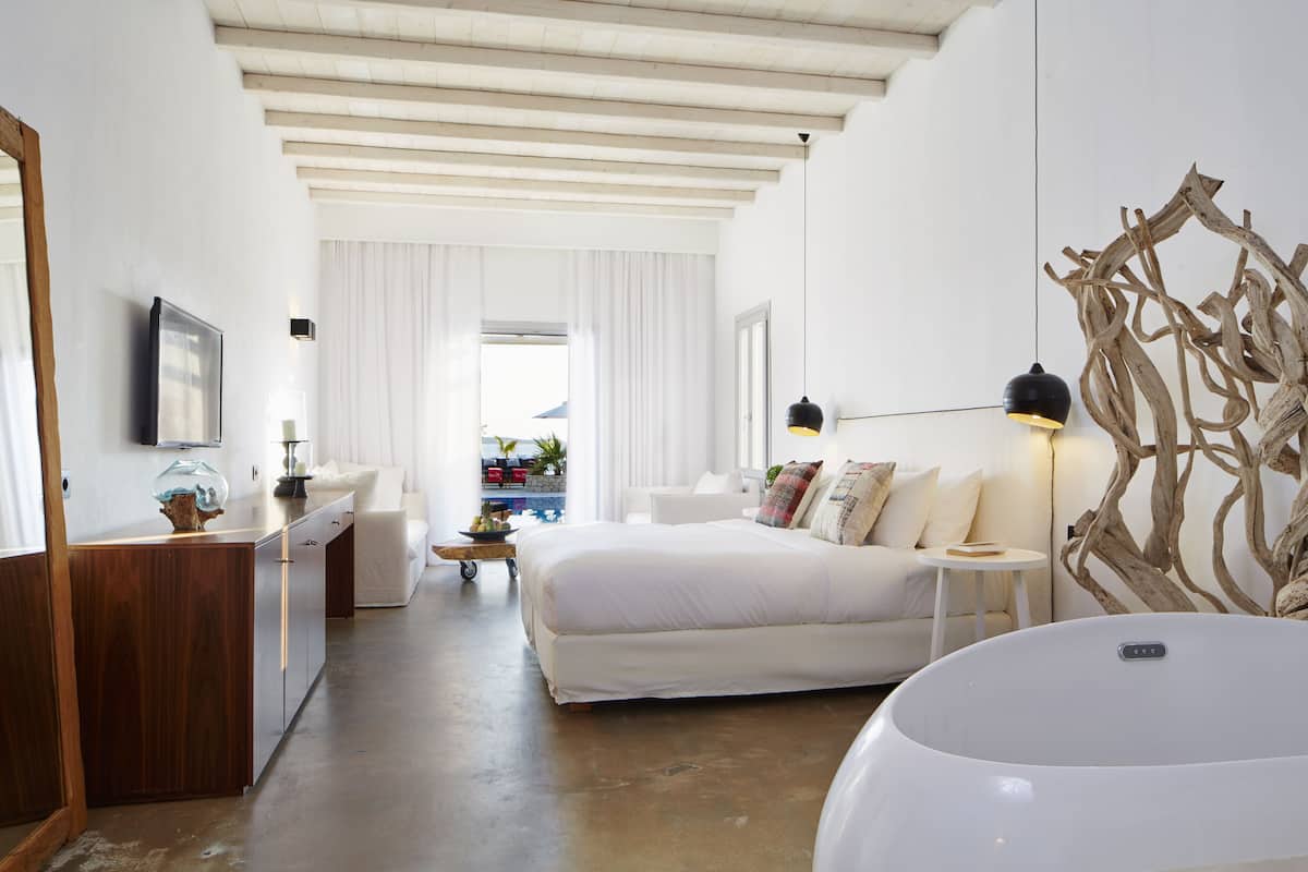 A modern bedroom with a large bed, a desk, and a vanity. There is a view of the outside through a window.