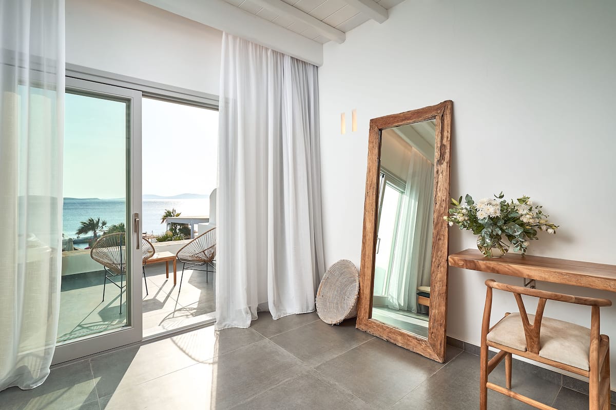 A room with a view of the sea, a large mirror, a wicker basket, and a wooden table.