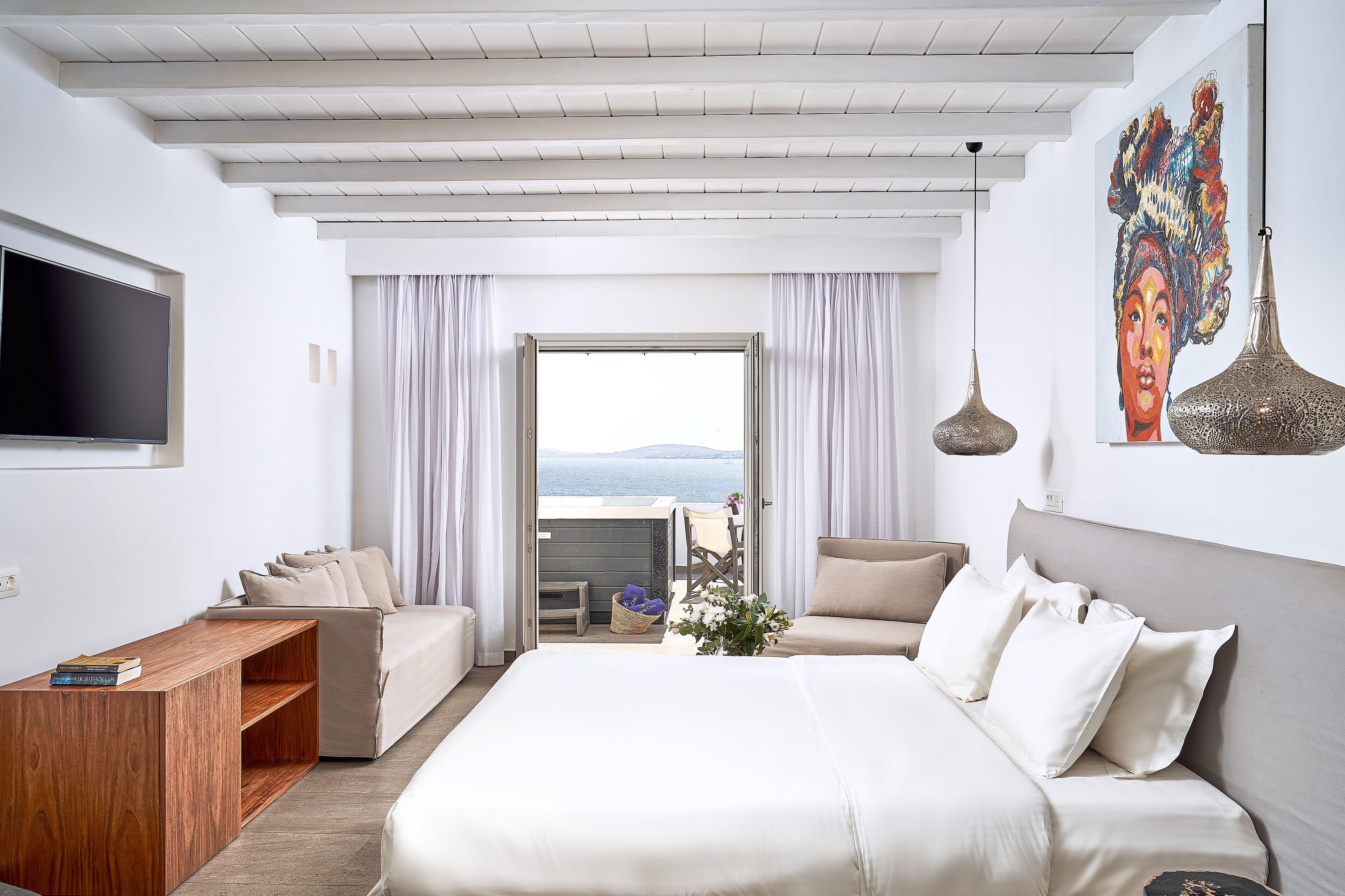 A modern hotel room with a large bed, a wooden desk, a flat-screen TV, and a balcony with a view.