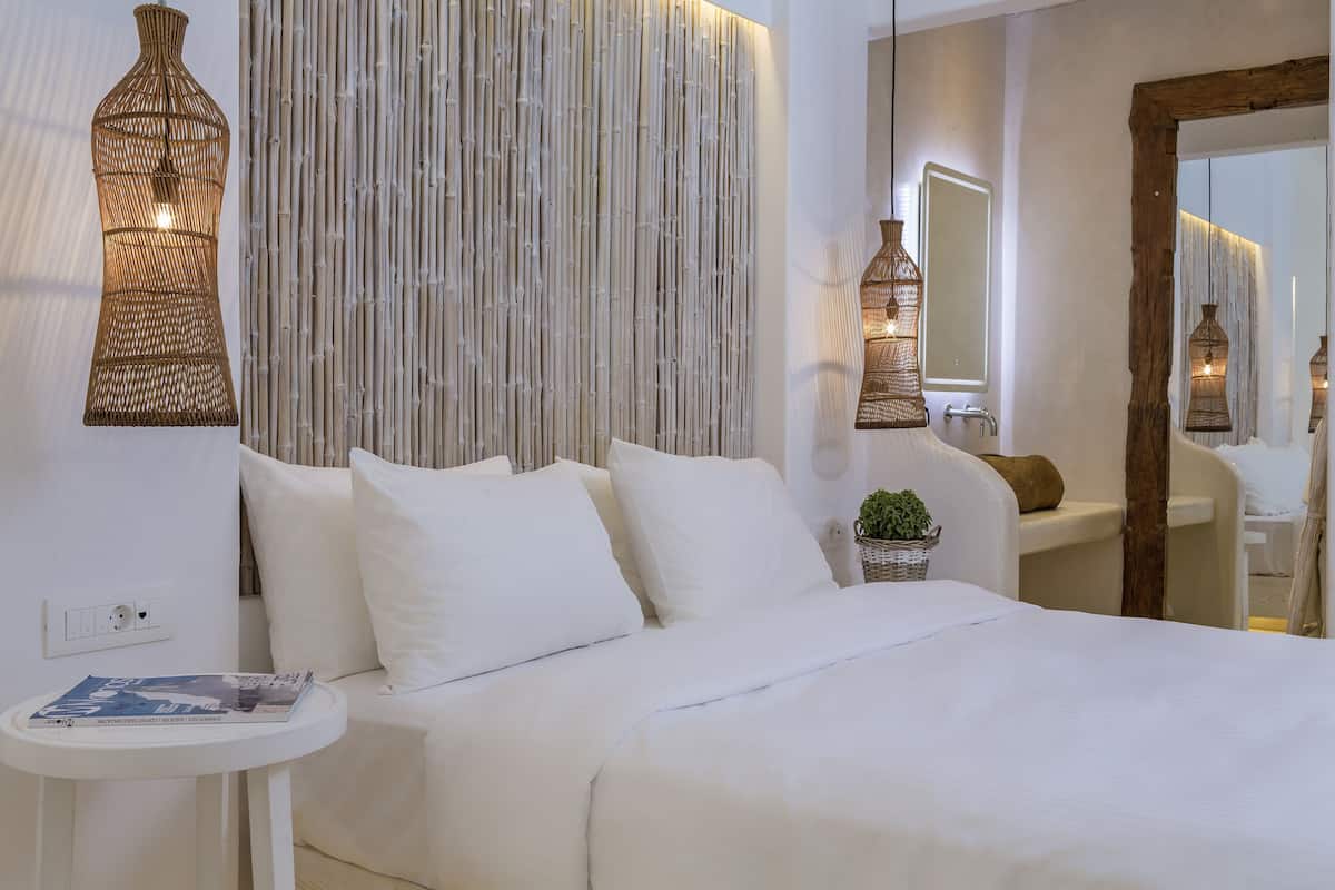 A modern bedroom with a large bed, a bedside table with a magazine, a wall-mounted mirror, and a vertical bamboo wall panel.