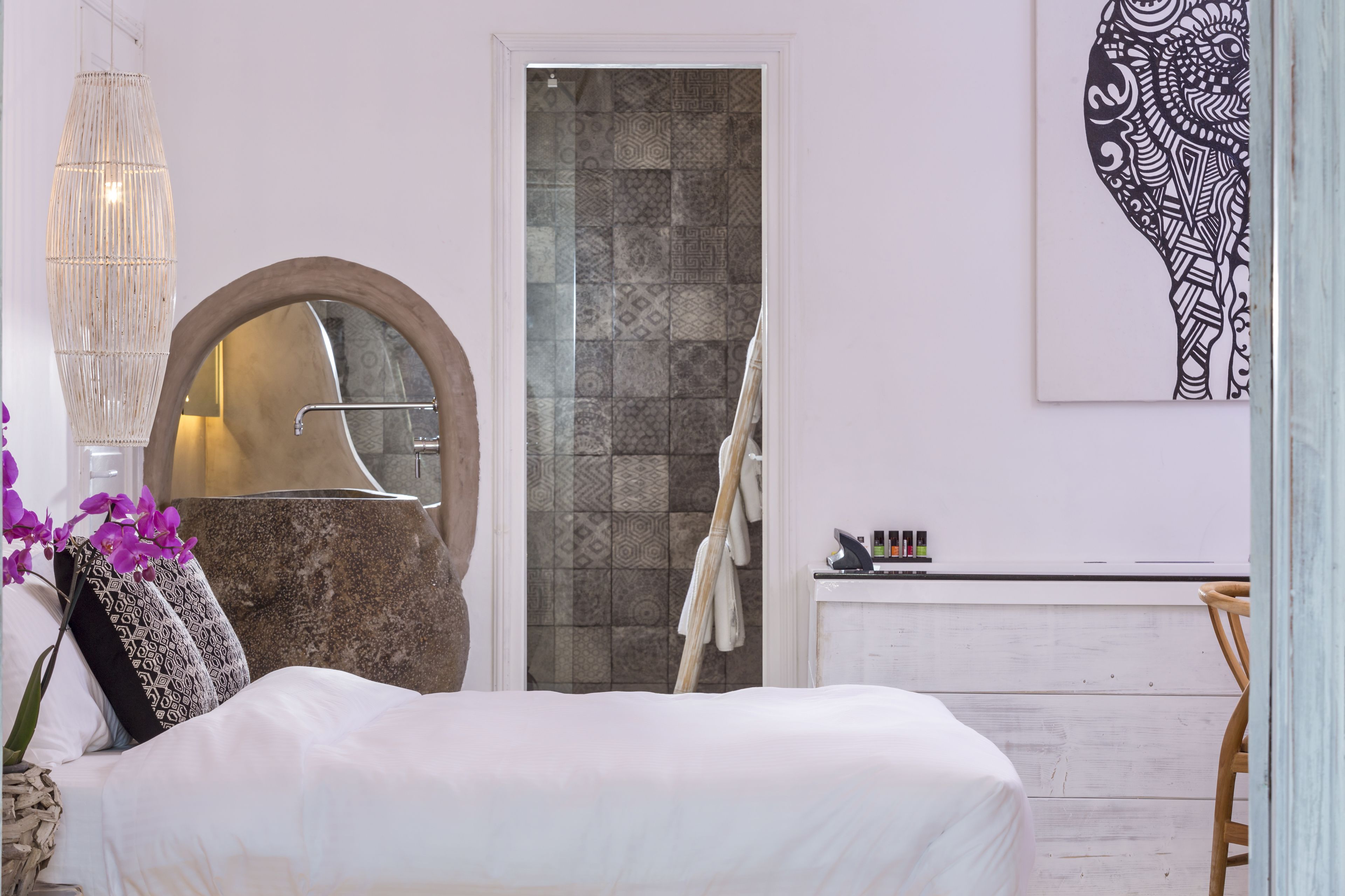 A bedroom with a bed, a large mirror, a shower, and a bathroom counter.