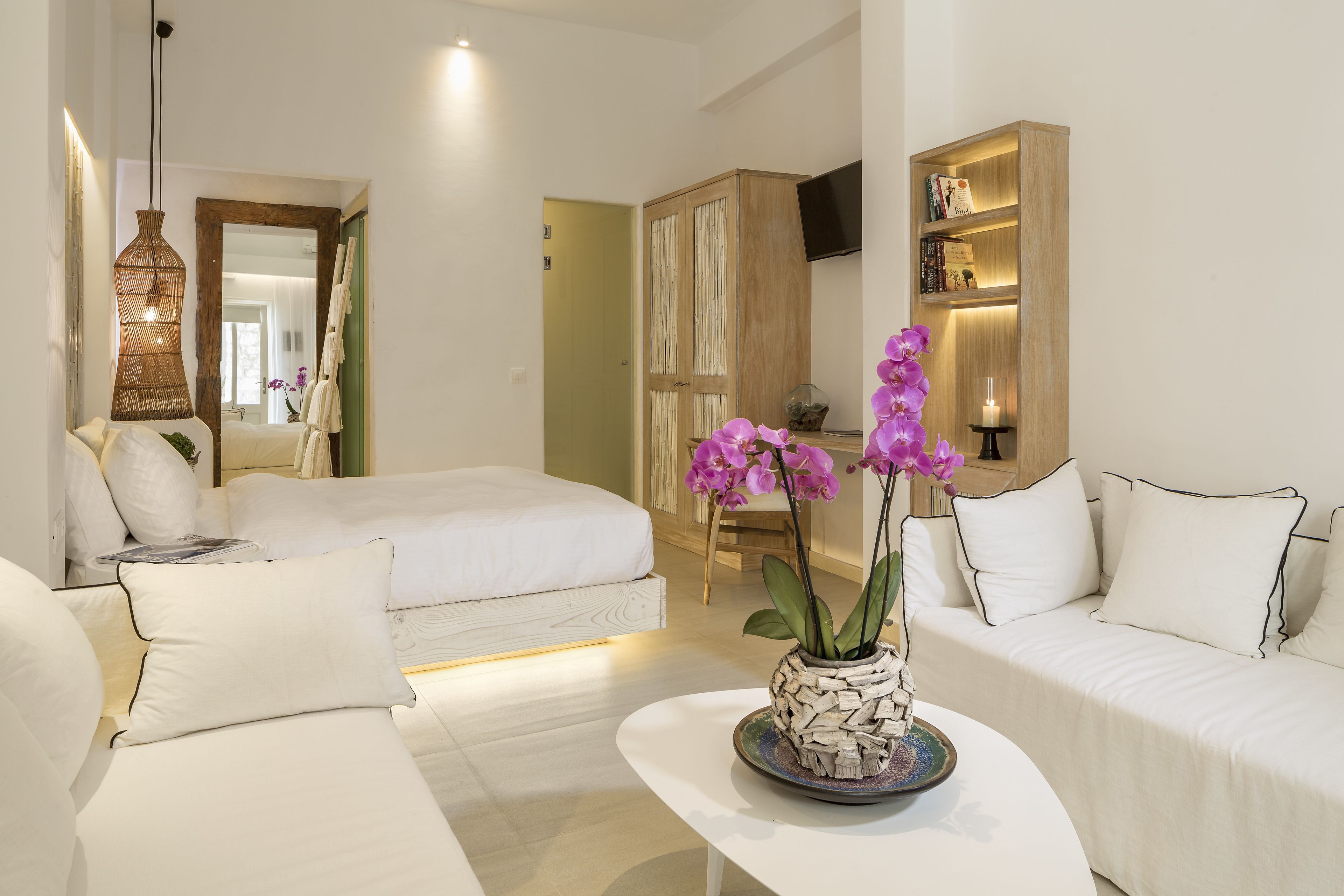 Una habitación de hotel moderna con una cama, un sofá blanco, una mesita y una planta de orquídea decorativa.
