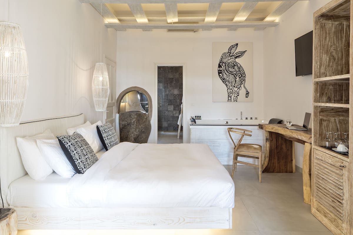 A bedroom with a large bed, a wooden desk, and a bathroom visible through an open door.