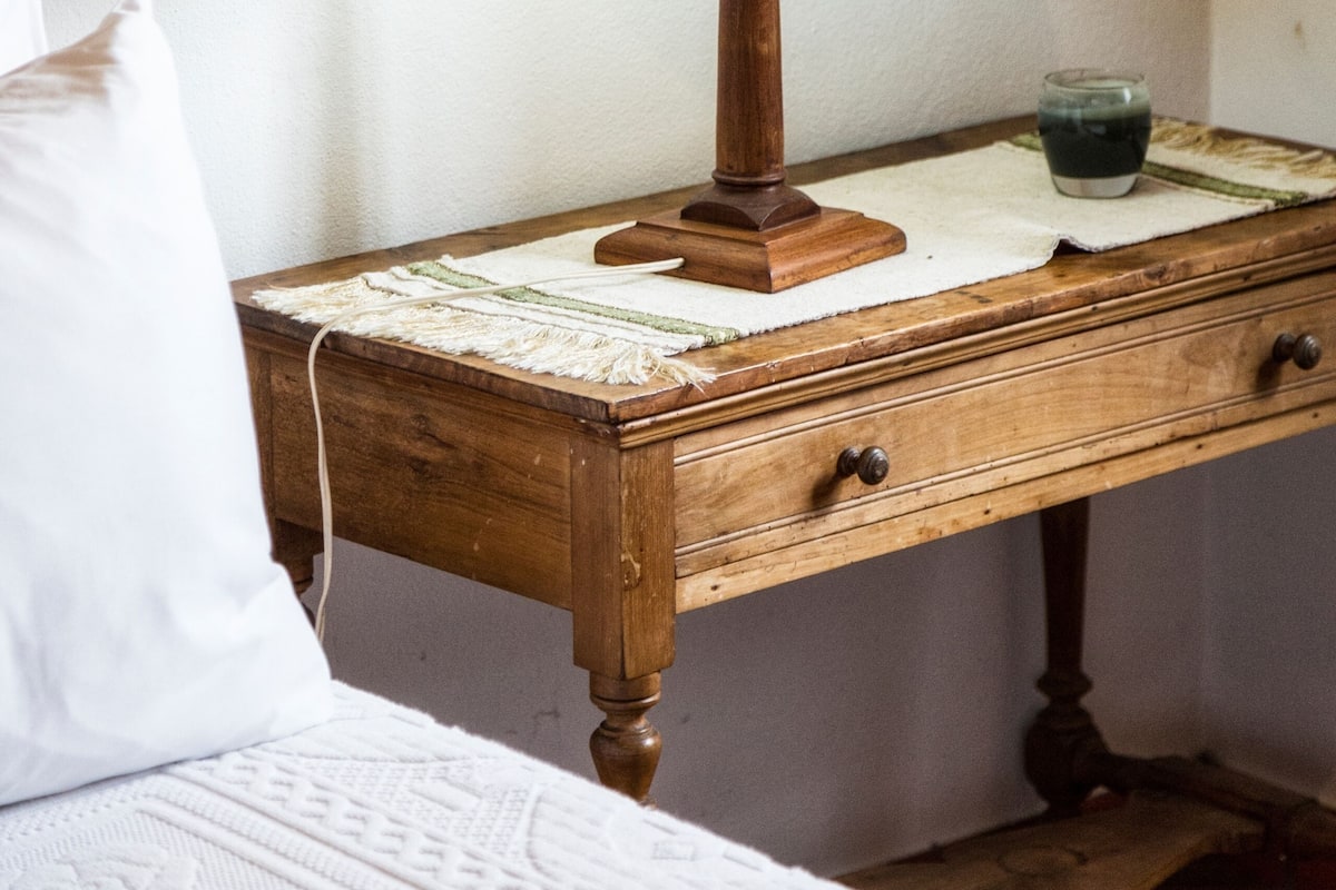 A wooden bedside table with a lamp, a glass, and a white pillow.