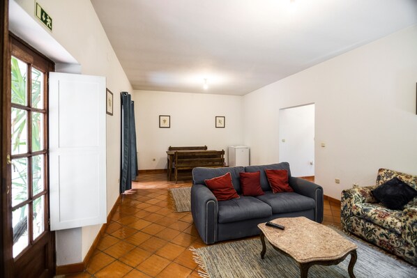 Una sala de estar con un sofá, un sillón estampado, una mesa de centro, un piano y una puerta con ventana.