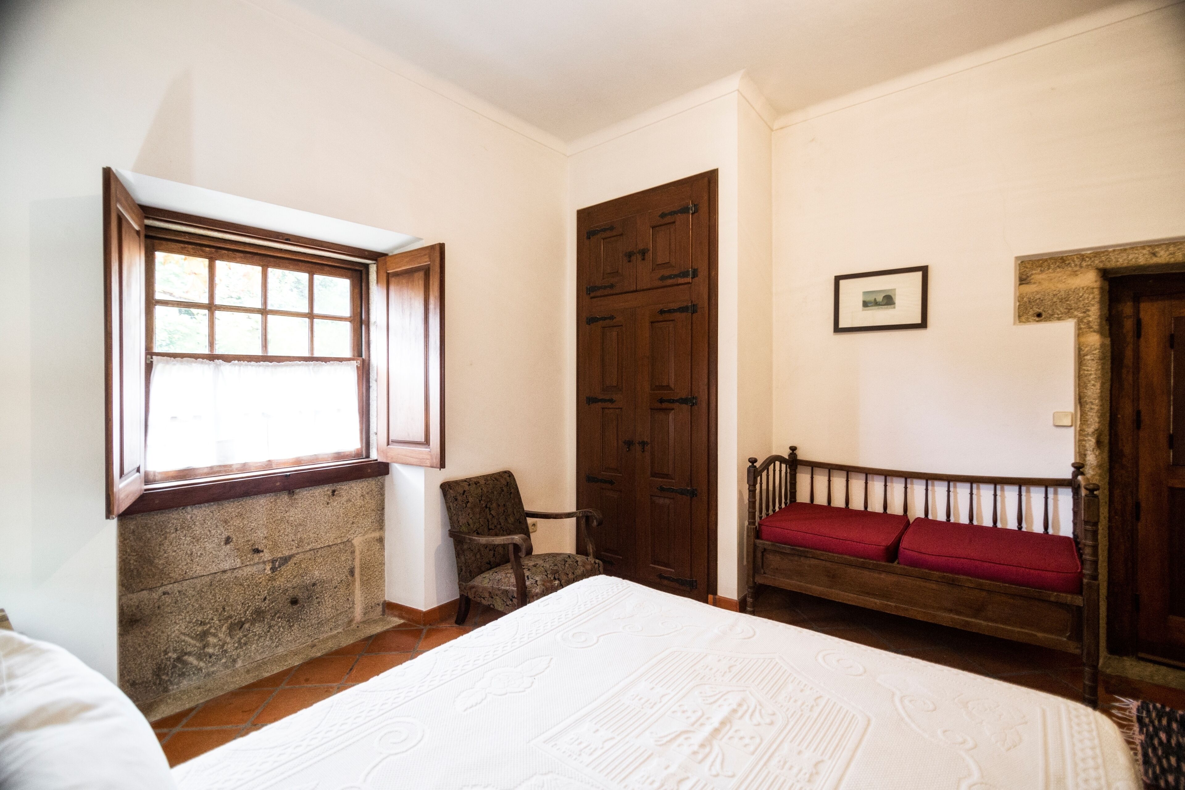 Ein Schlafzimmer mit einem großen Bett, einem Holzschrank, einem Sessel und einer Bank mit roten Kissen.