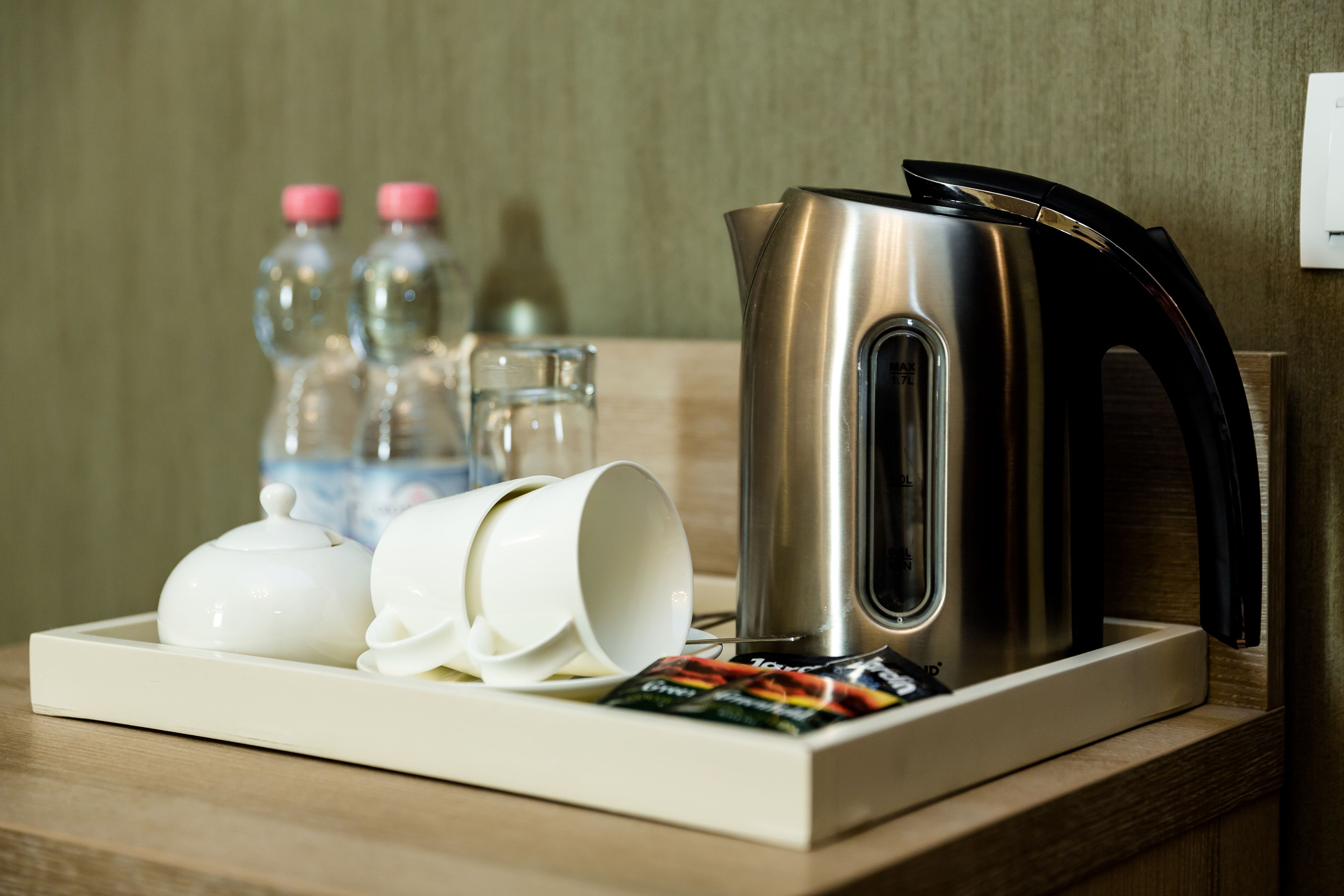 A tray with a teapot, two cups, two bottles, and a packet of tea on a wooden table.