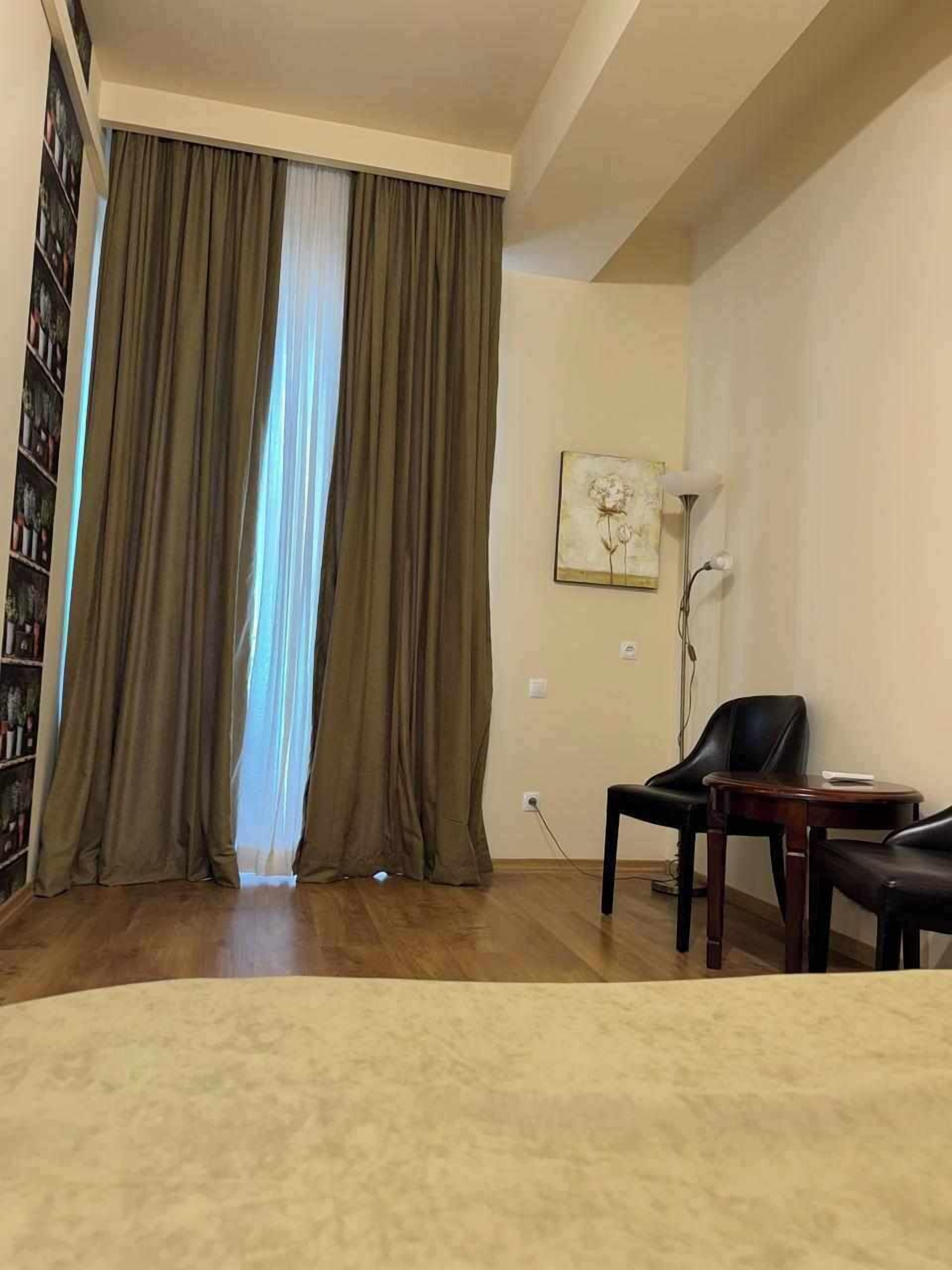 Una habitación de hotel con un ventanal grande, una estantería, un cuadro y dos sillones.