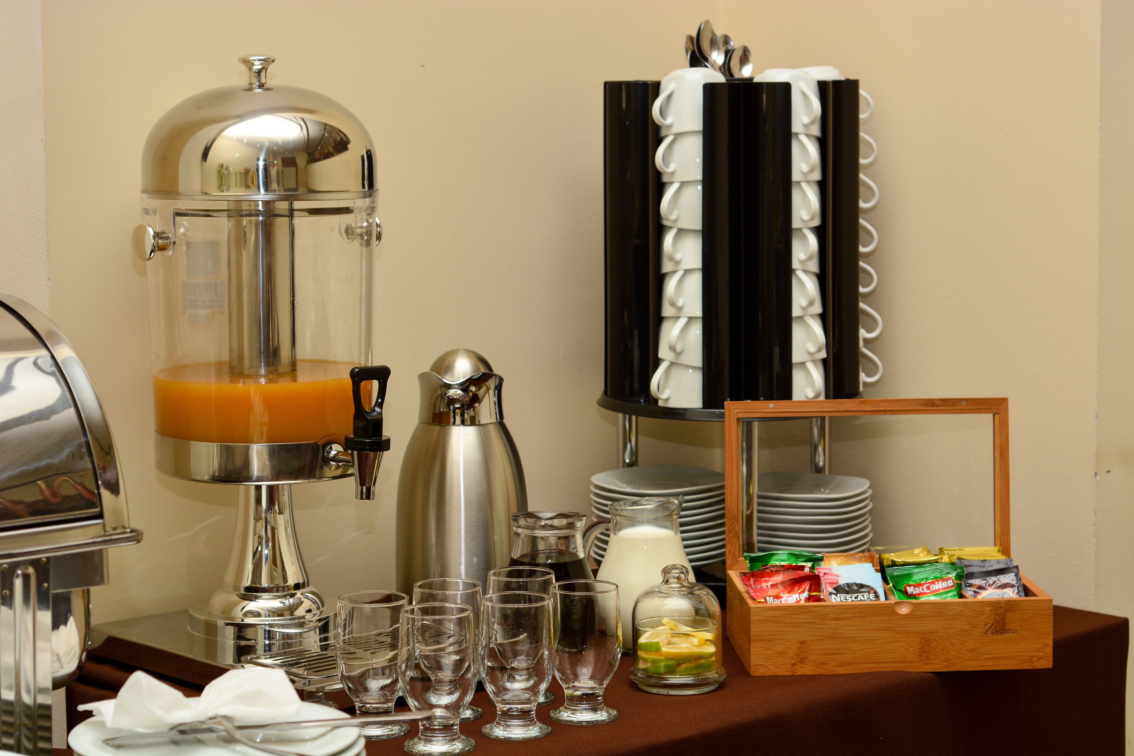 A breakfast buffet setup with a coffee maker, juice dispenser, and a variety of food items.