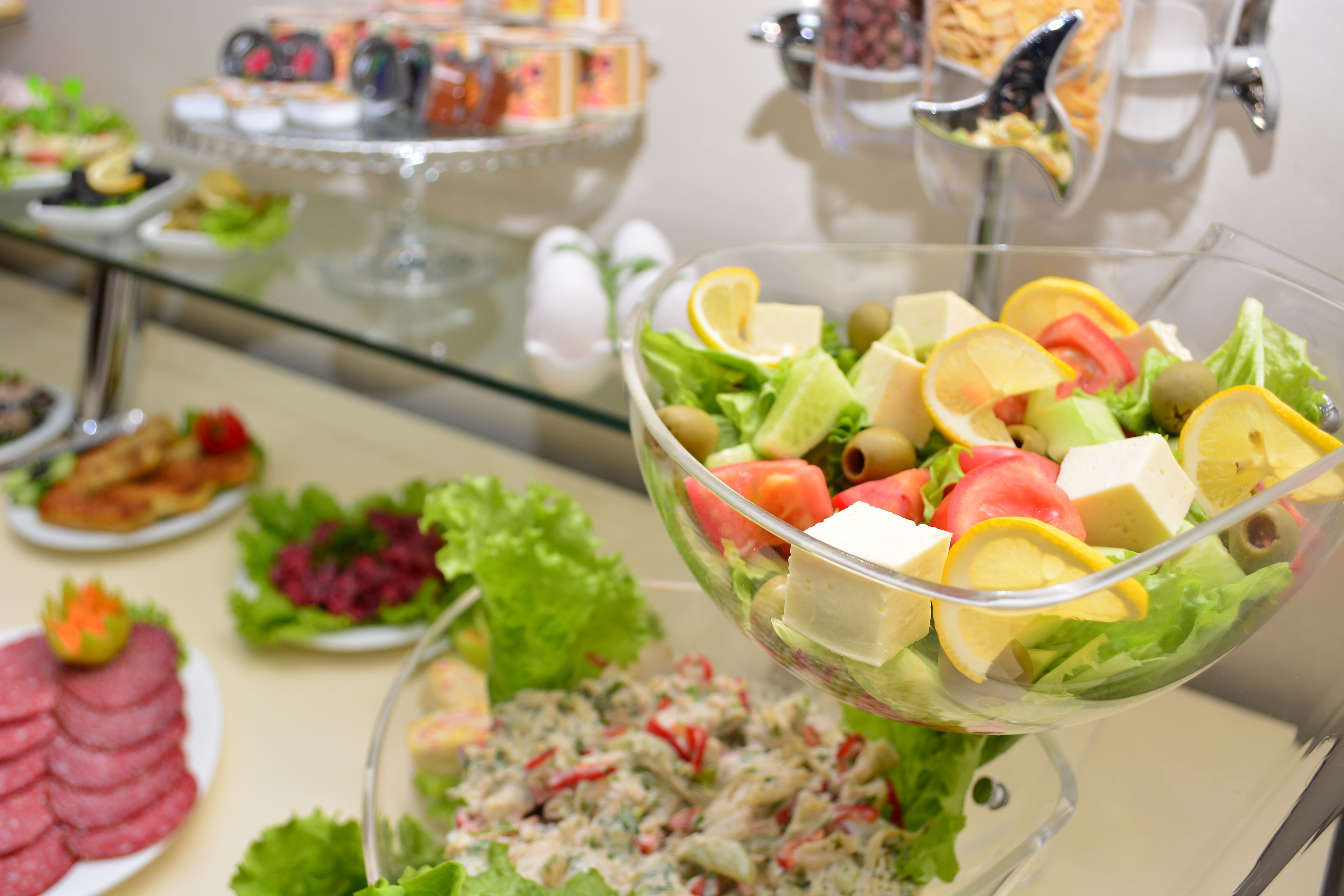 A buffet with various dishes including a salad bowl with vegetables and cheese, and other food items on plates.