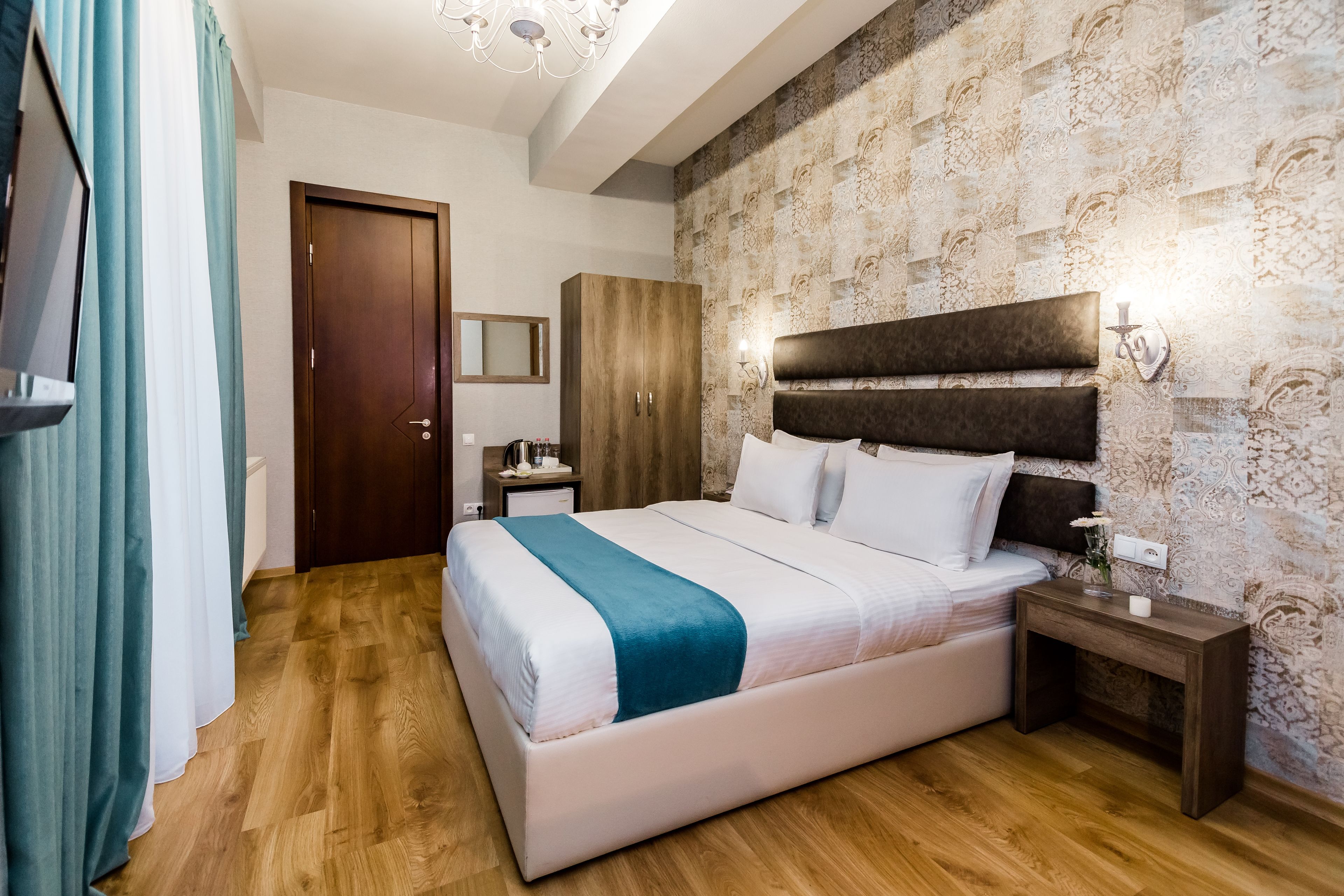 Une chambre à coucher avec un grand lit, un plancher en bois, une armoire, une table de chevet avec une lampe et un miroir au mur.