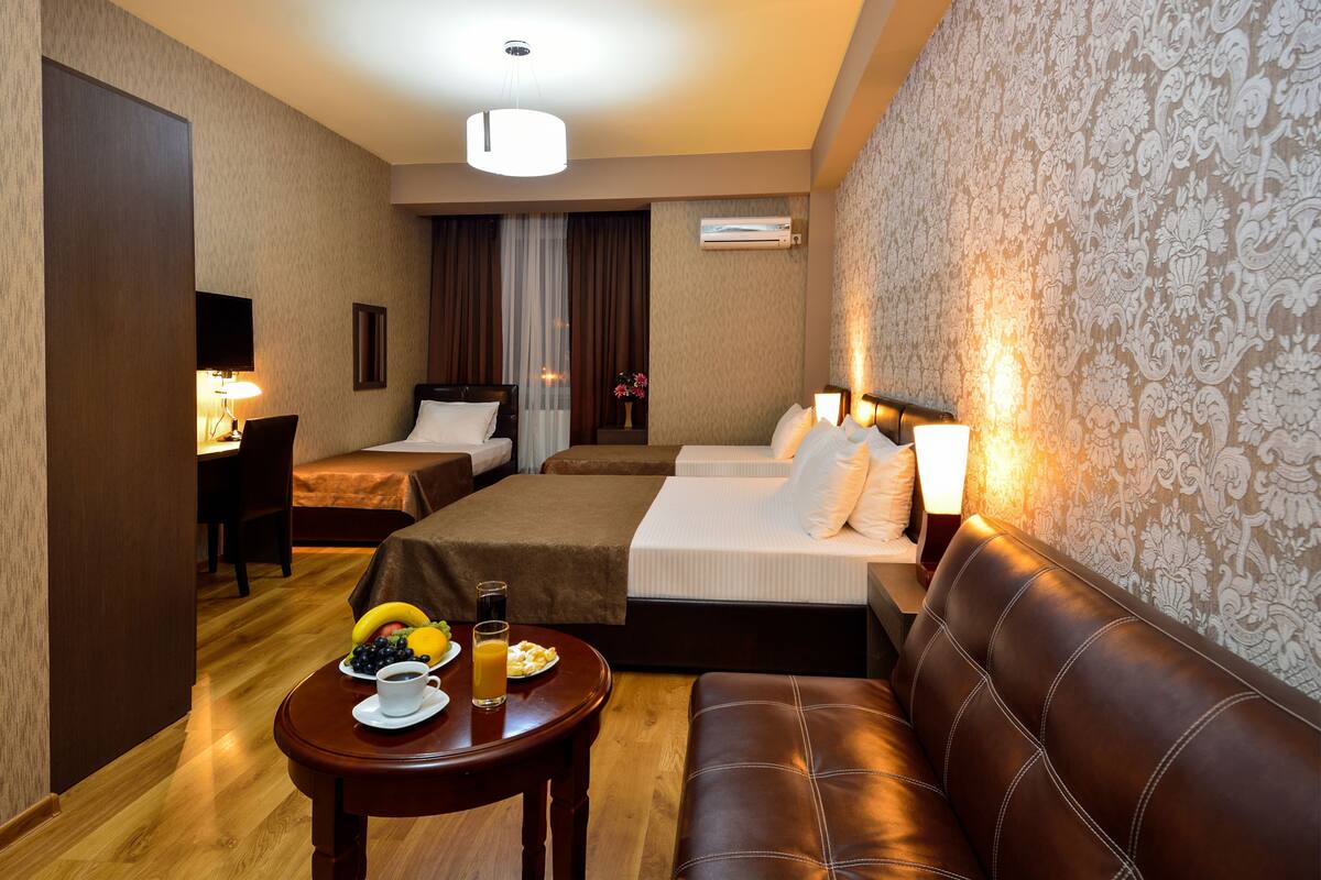 Habitación de hotel con dos camas, un sofá, una mesa de comedor con desayuno y un ventanal grande.