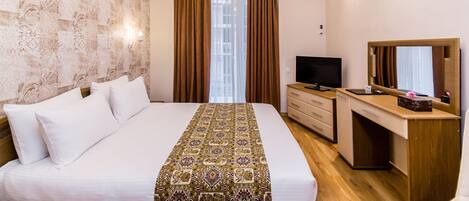 Quarto de hotel com uma cama grande, uma escrivaninha com televisão e um espelho.
