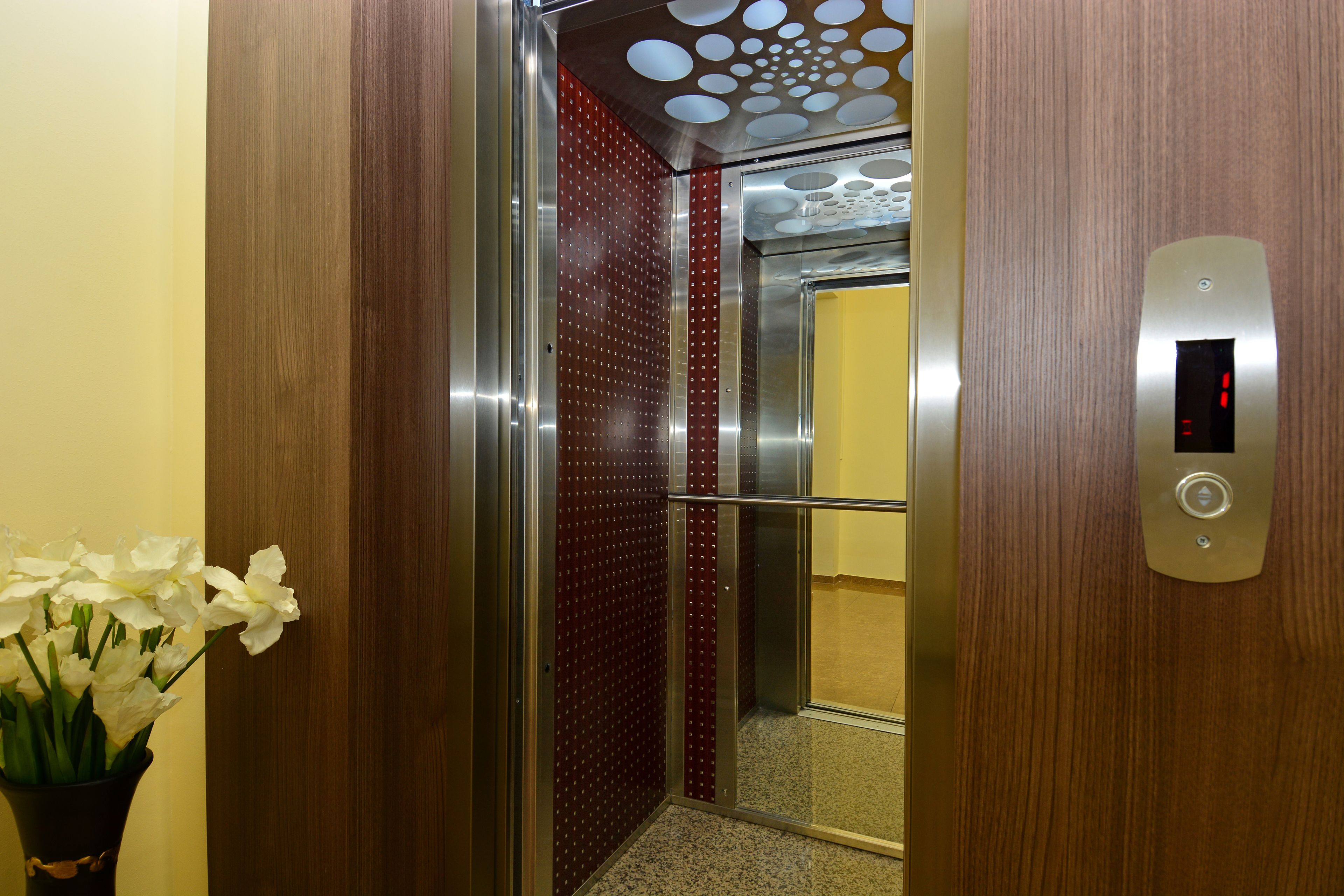 Een liftinterieur met een houten afwerking, een metalen bedieningspaneel en een glazen deur.