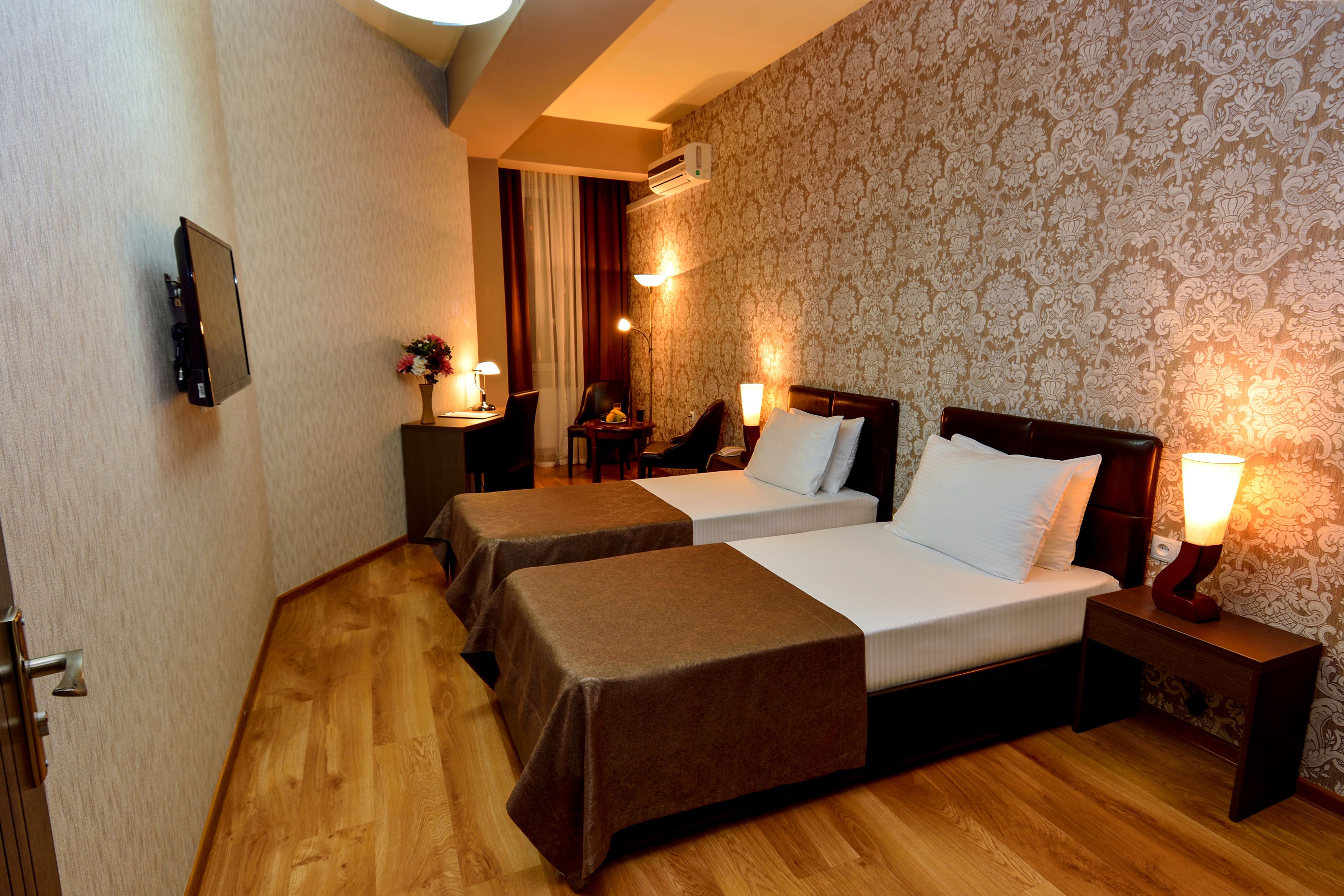 A hotel room with two beds, a desk, a chair, a lamp, and a TV.