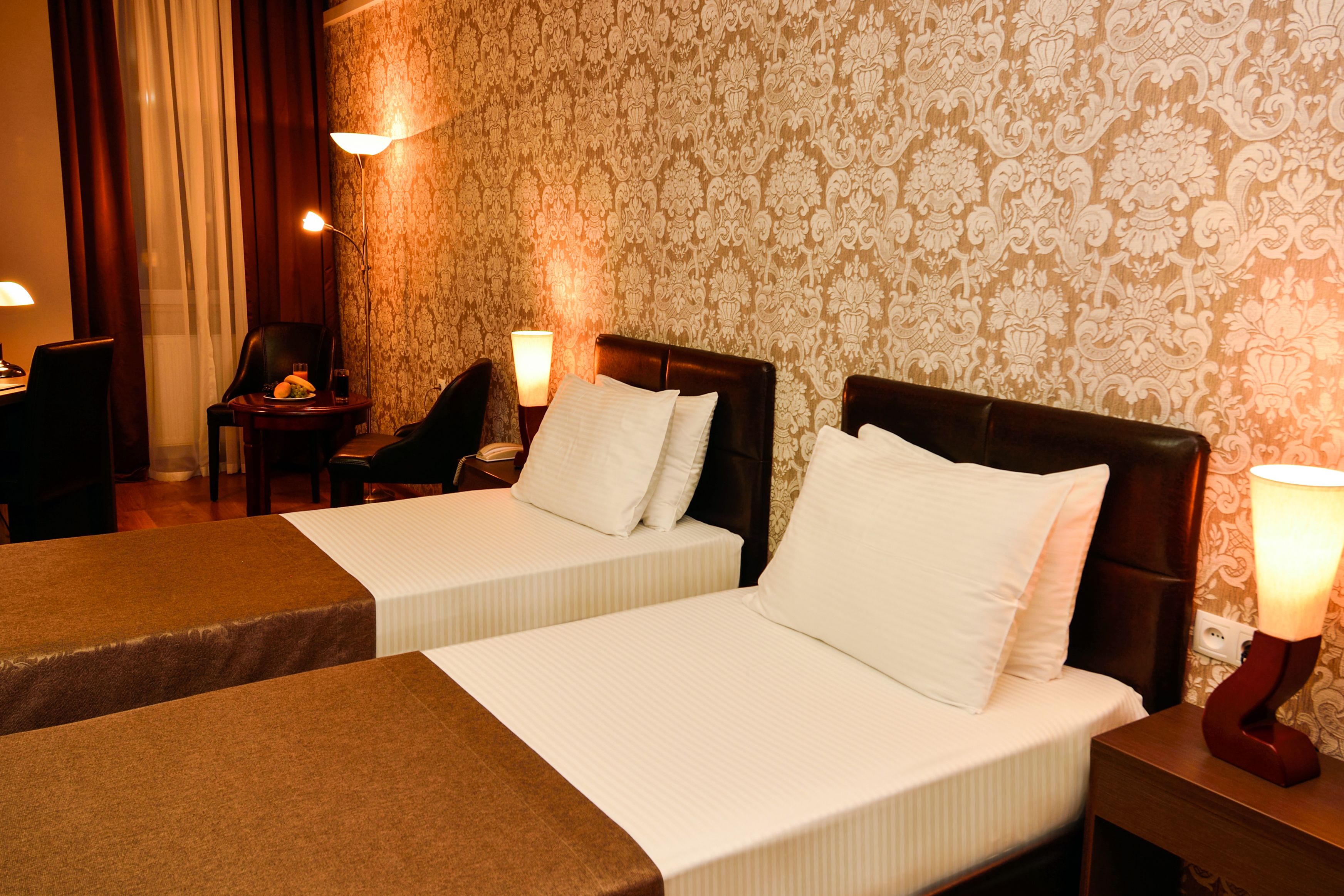 A hotel room with two single beds, a chair, a small table, and a lamp.