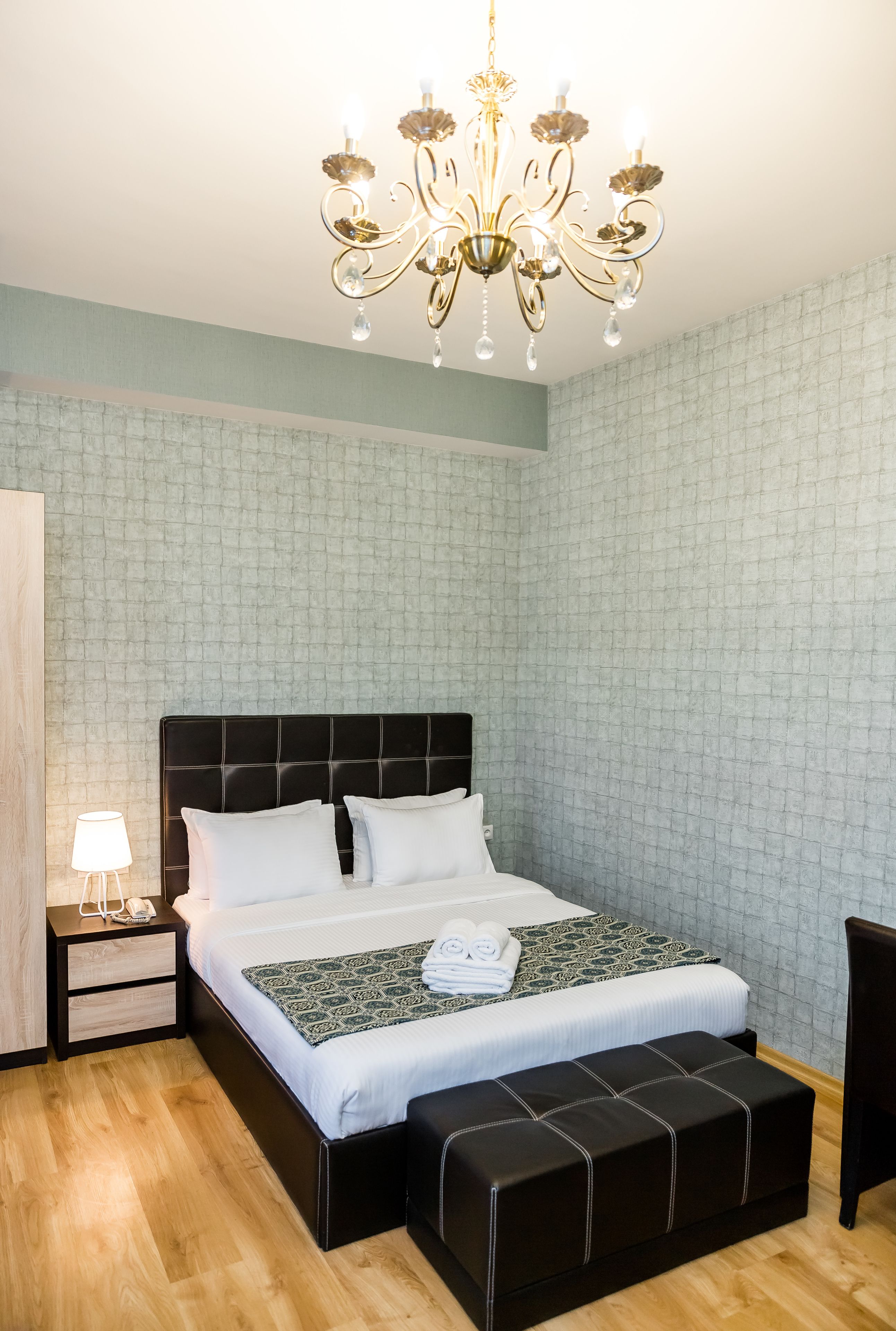 Un dormitorio ordenado con una cama grande, una mesita de noche con lámpara, un banco y una araña.