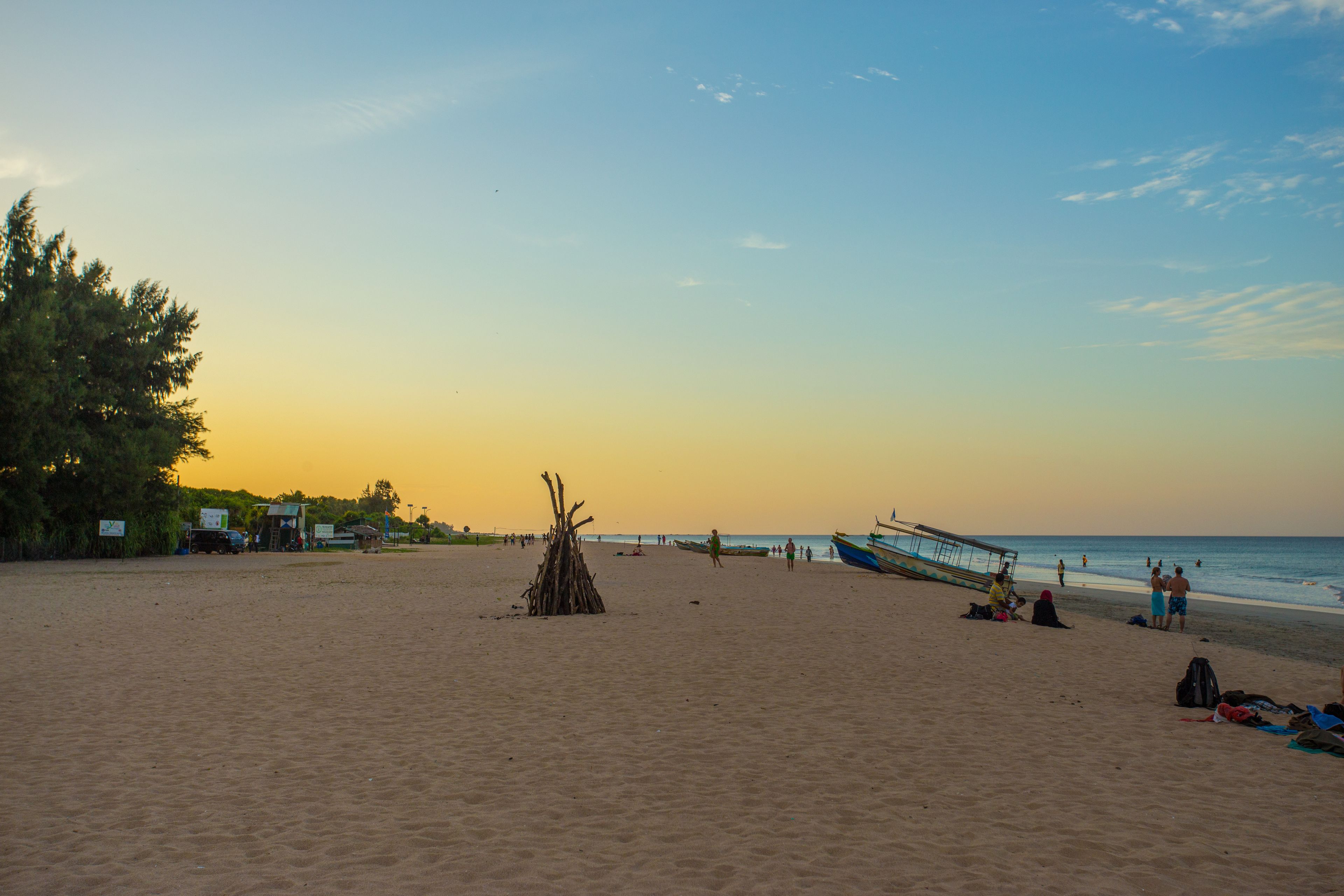 Una playa con una estructura de madera, un bote y gente.