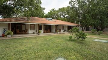 A two-story building with a tiled roof, a covered patio area with wooden furniture, and a well-maintained lawn.
