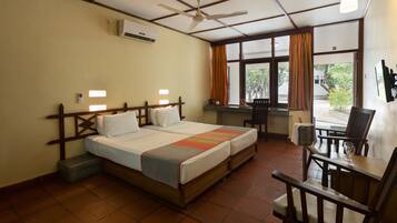 A hotel room with a bed, a desk, a chair, a window with curtains, and a ceiling fan.