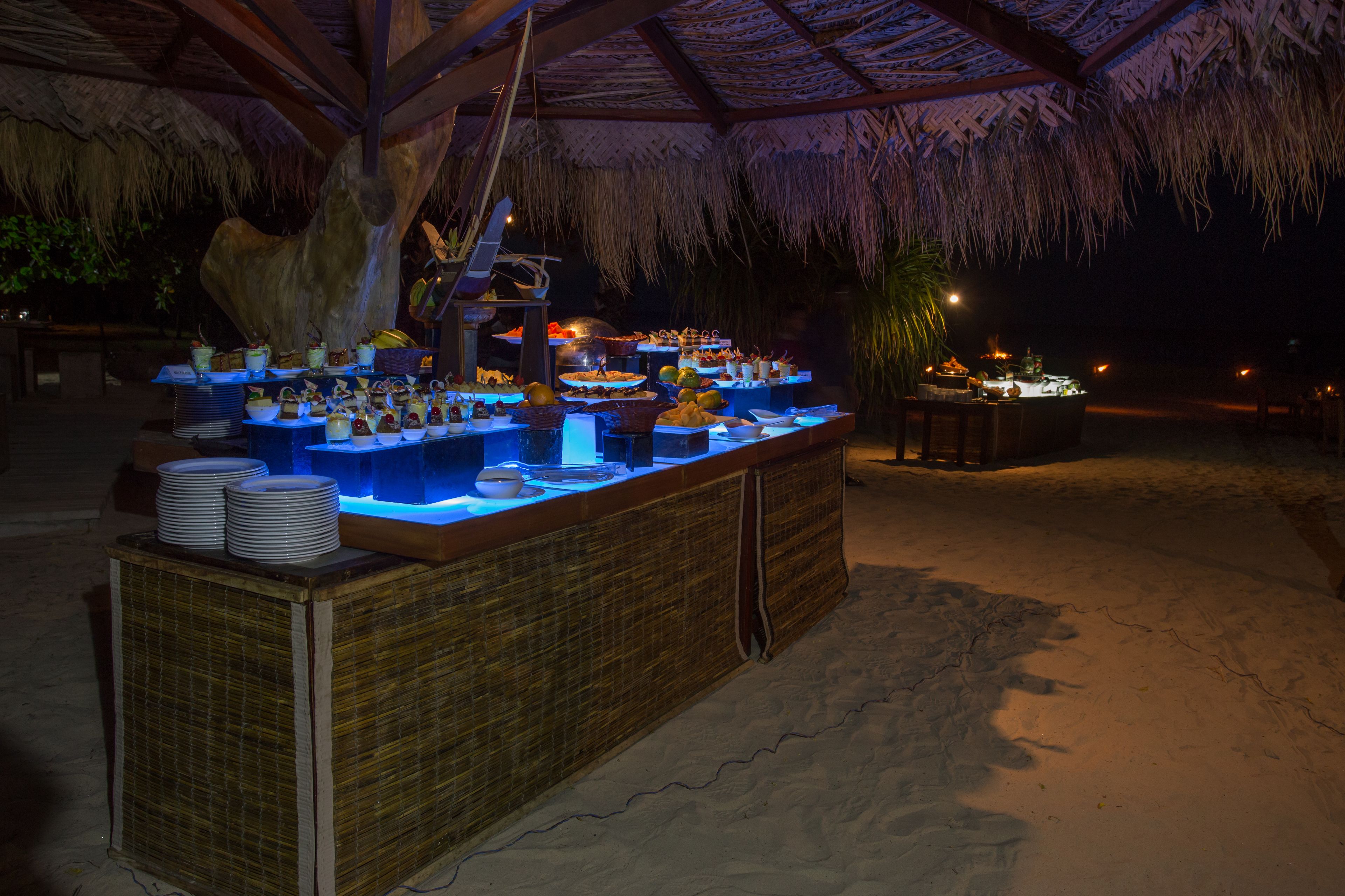 Un buffet proposant une variété de plats et de boissons, installé sous un toit de chaume.