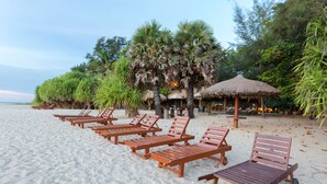 Une plage avec des chaises longues en bois et des structures à toits de chaume.