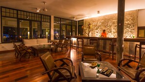 Un espace lounge moderne doté d’un plancher en bois, de fauteuils en cuir, d’une table basse en verre et d’un comptoir de bar avec un barman.