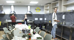A modern kitchen with a recycling sign, stainless steel appliances, and a dining area with tables and chairs. - Micampus Galileo Galilei (Valencia)