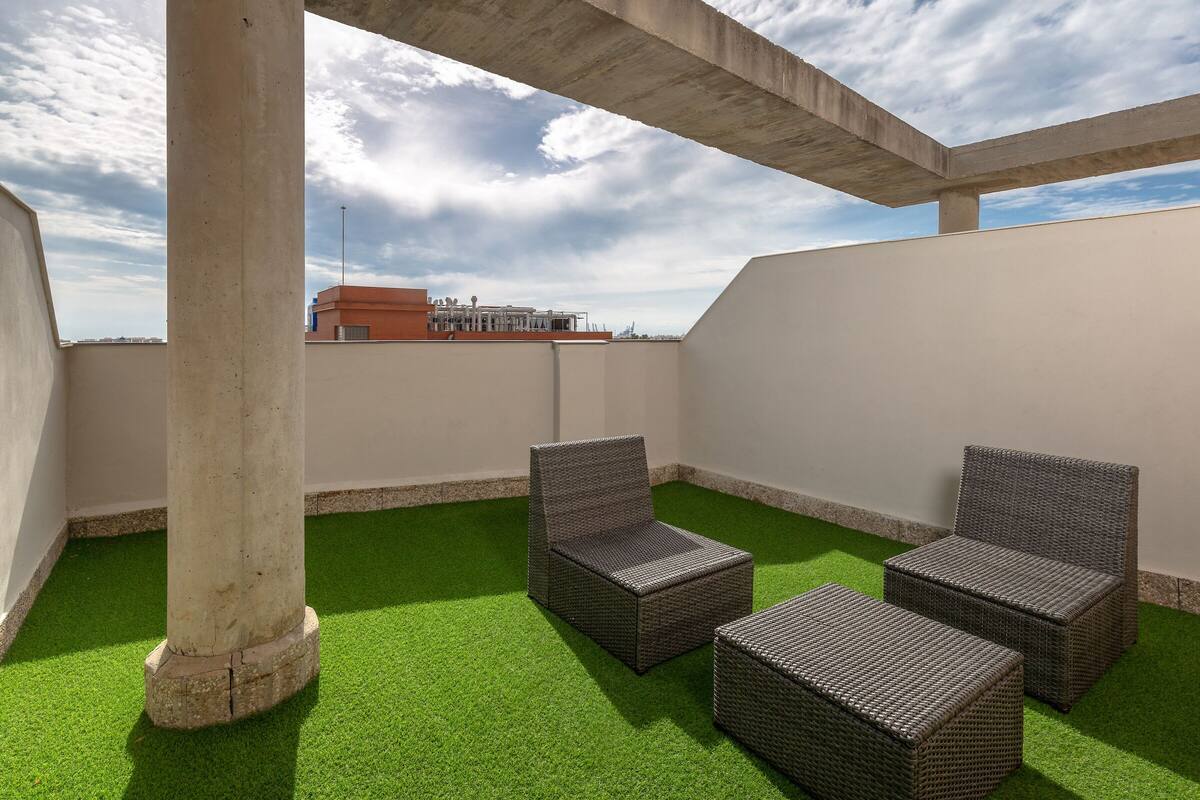 Une terrasse sur le toit, avec un revêtement de gazon synthétique, deux fauteuils en osier et une structure en béton.