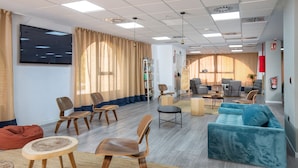A spacious living area with a large flat-screen TV, multiple seating options including sofas and chairs, a coffee table, and a bookshelf.