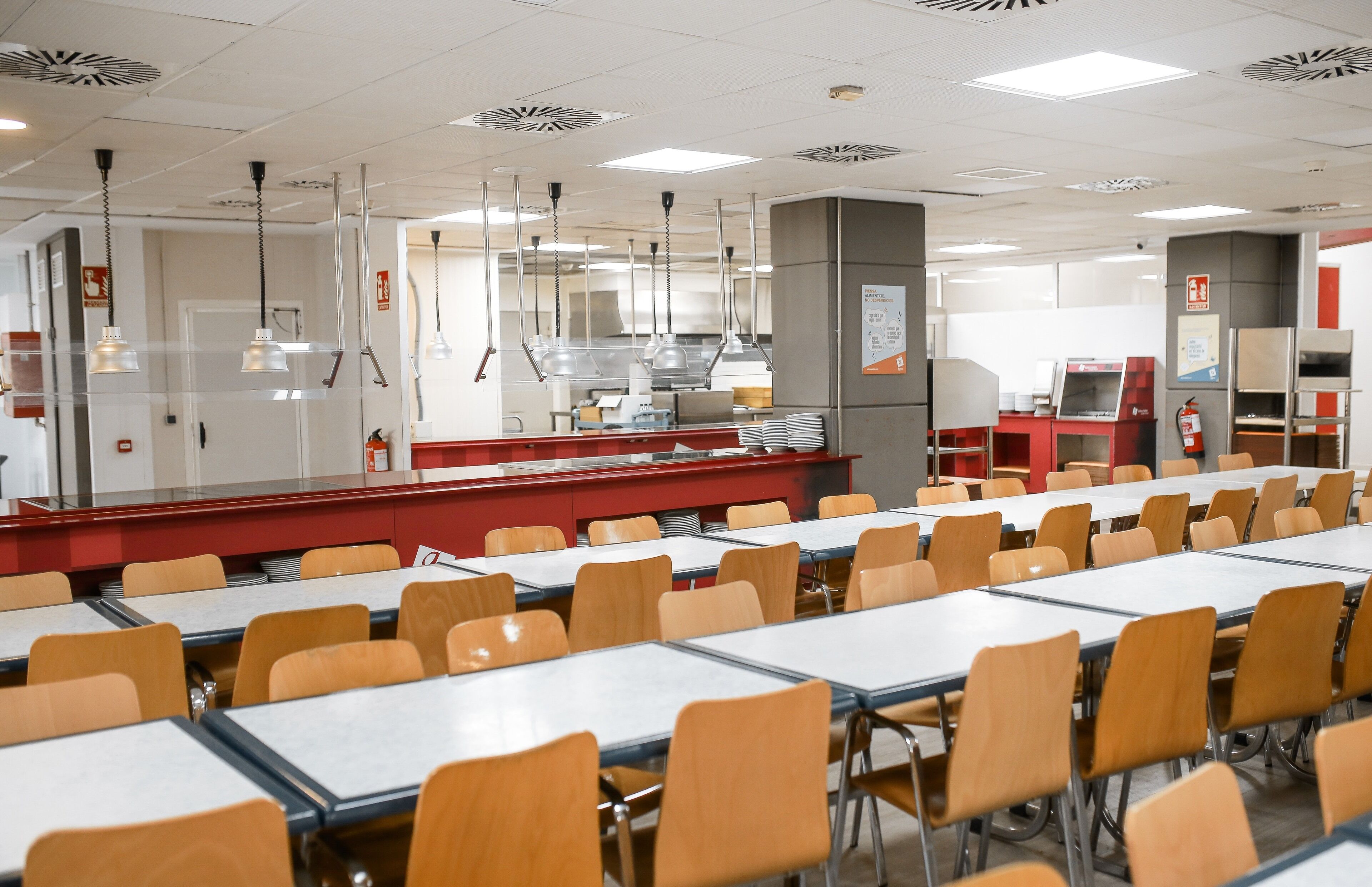 Una cafetería con mesas y sillas, una zona de cocina y un extintor.