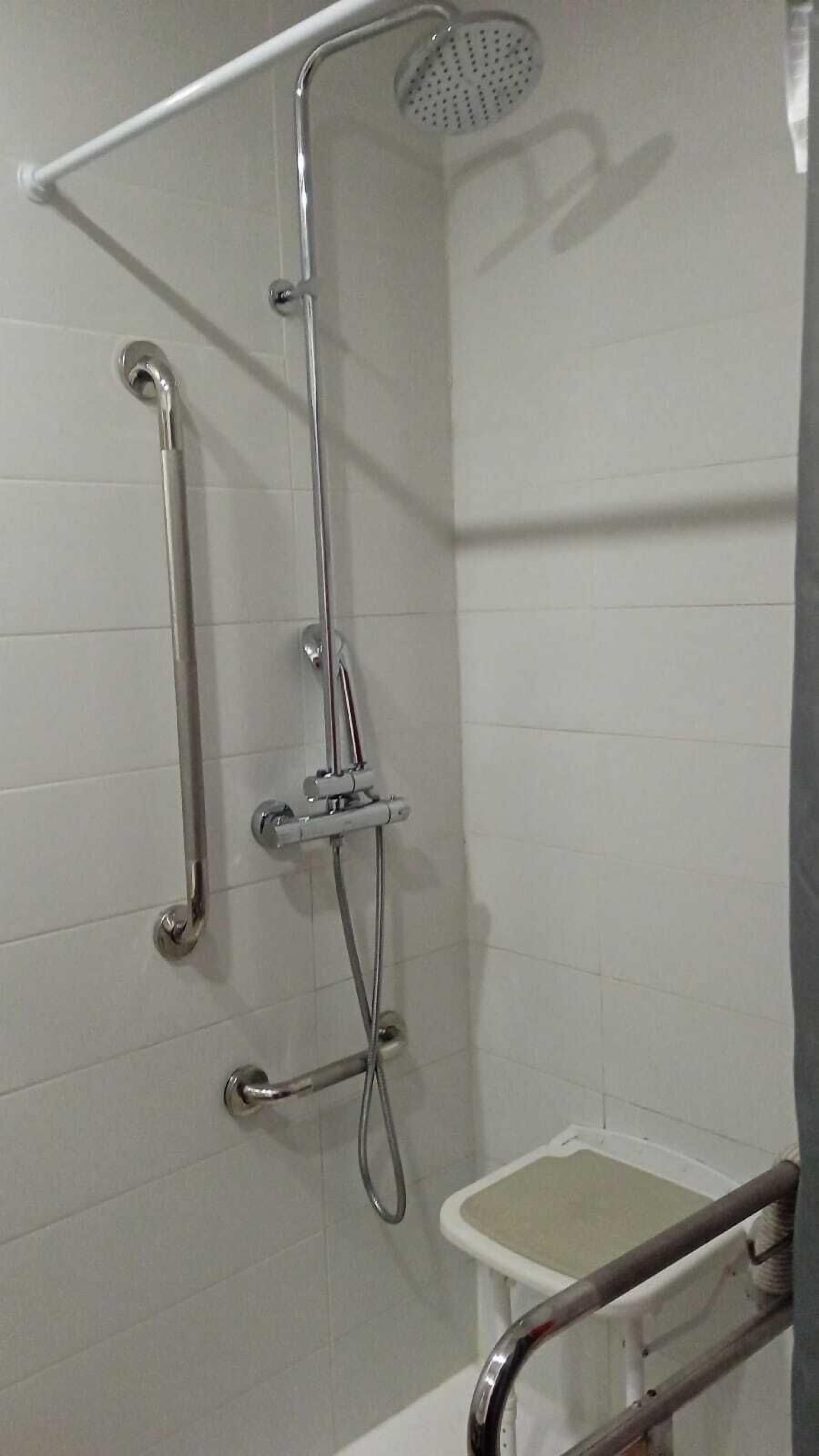 A shower area with a handheld showerhead, a handheld shower attachment, and a grab bar.