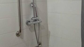 A shower area with a handheld showerhead, a handheld shower attachment, and a grab bar.