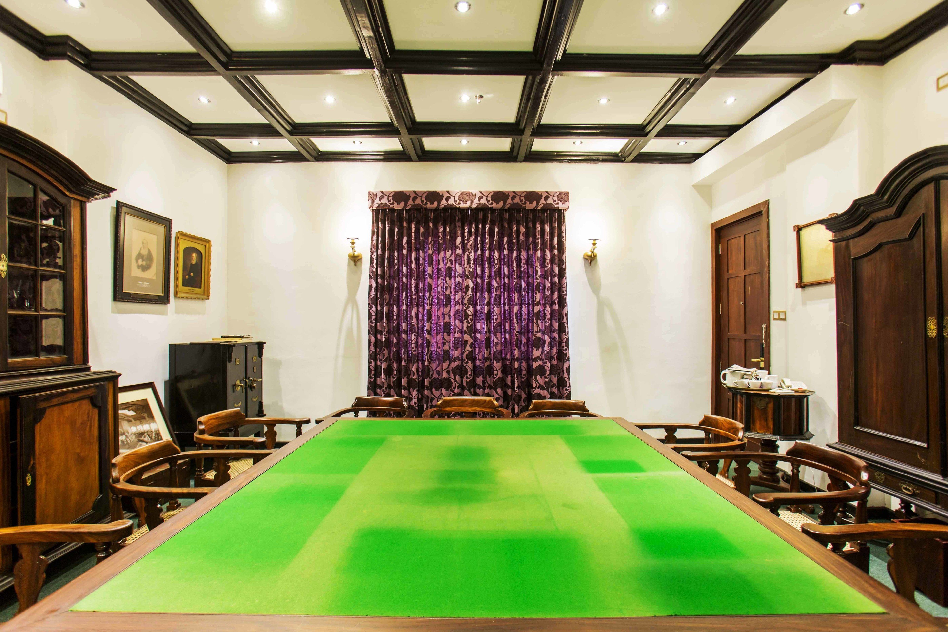 A conference room with a long table, wooden chairs, a patterned curtain, and framed pictures on the walls.