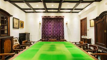 A conference room with a long table, wooden chairs, a patterned curtain, and framed pictures on the walls.