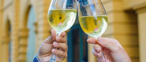 Dos personas brindando con copas de vino frente a un edificio con ventanas de arco y un letrero de neón.