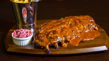 A plate with a meat dish and a small bowl of red sauce, accompanied by a bucket of fries.