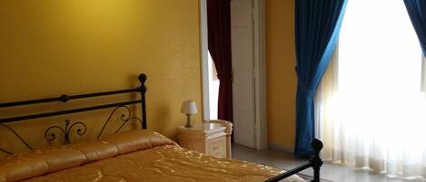 Une chambre à coucher comprenant un lit, une table de chevet, une lampe et une porte donnant sur une autre pièce.