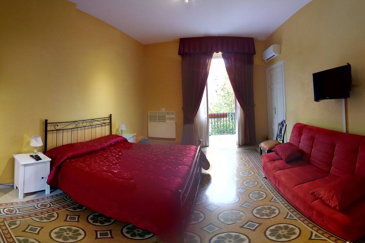 Ein Hotelzimmer mit Bett, einem roten Sofa, einem Fernseher und einem Fenster mit Vorhängen.